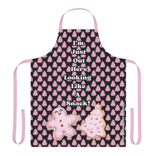 A pink apron with black background featuring text and images related to Christmas, such as cookies and trees.